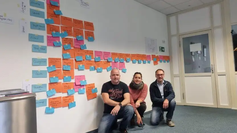 Drei Workshopteilnehmer*innen hocken vor einer Wand mit Post-Its